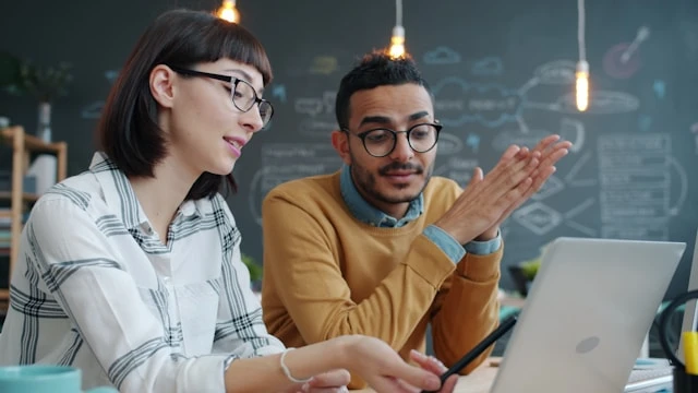 Two people discussing documents together at a laptop