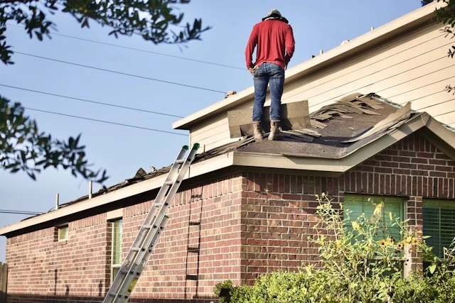 Inspector standing on the roof of a brick home with a ladder against the eave